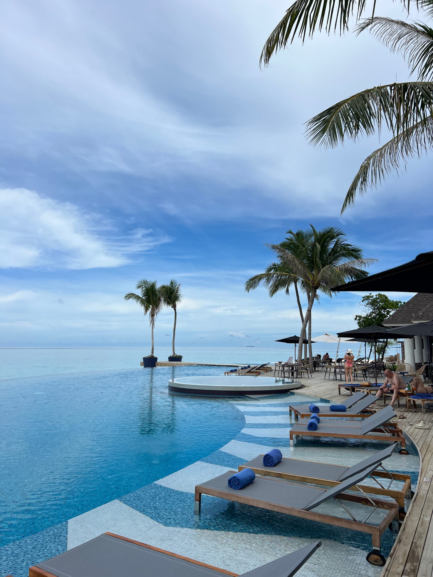 A Maldivian resort swimming pool, sunbeds and a view out to the sea