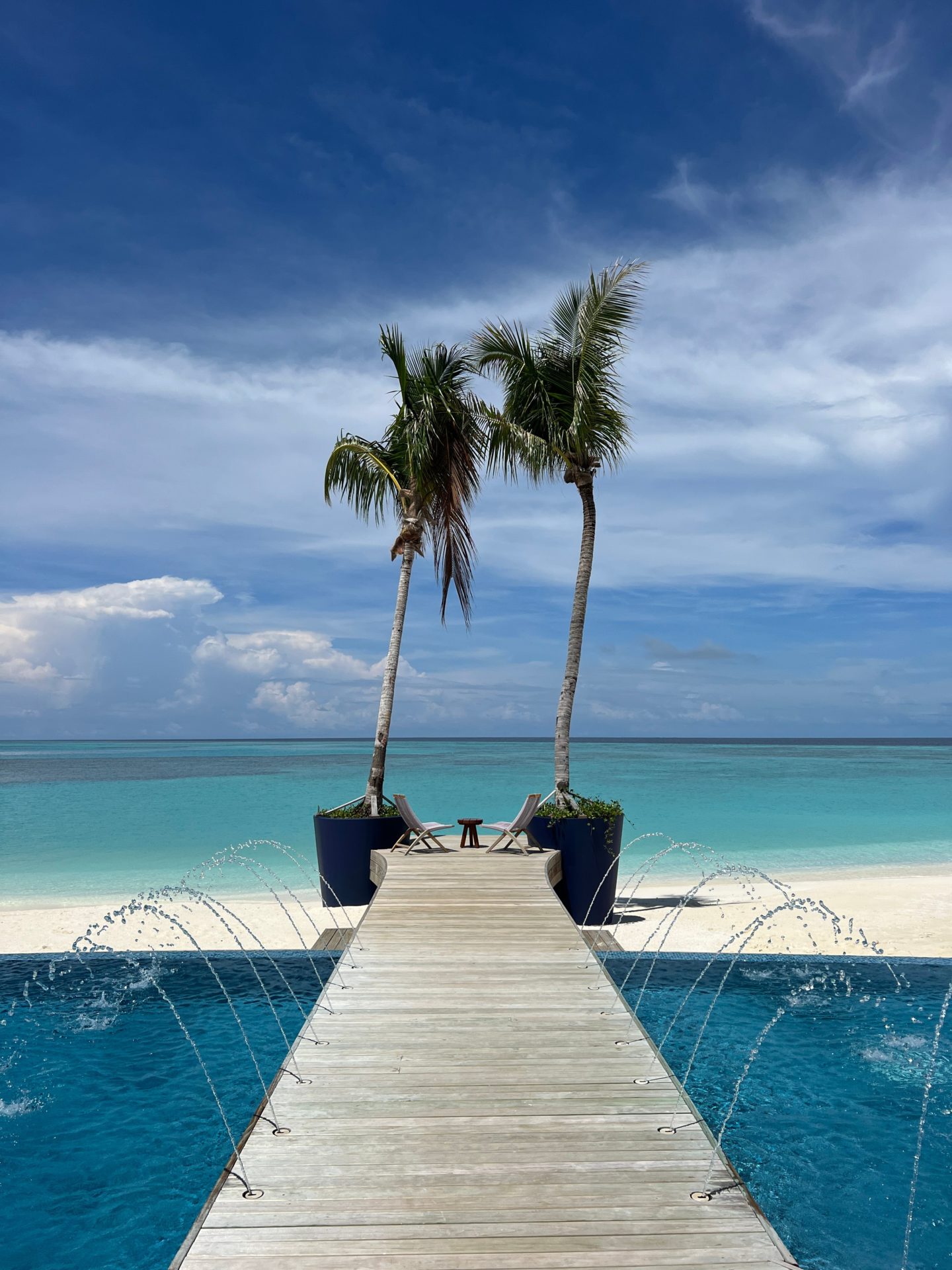 View of the sea in the Maldives looking out across a walkway, flanked by two palm trees