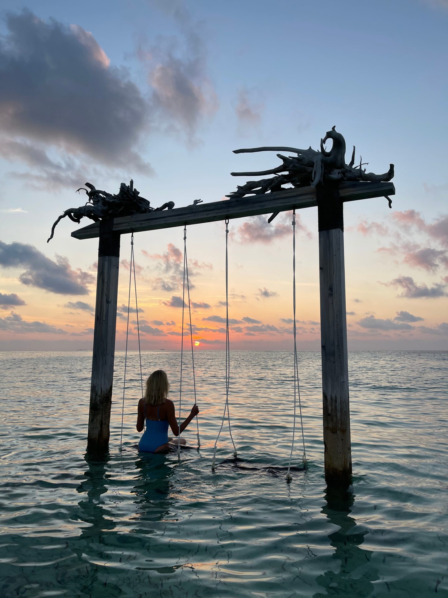 Zanna van Dijk sat on a swing in the middle of the sea in the Maldives looking out to the horizon at dusk