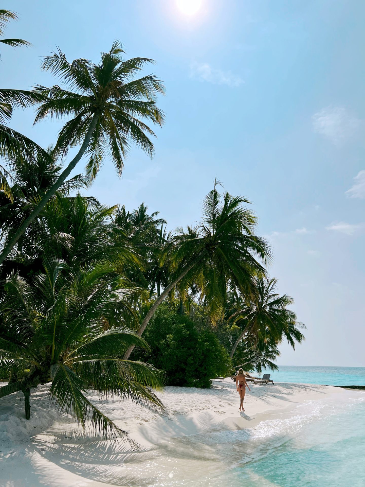 Zanna van Dijk walking along a Maldivian white sand beach lined with palm trees