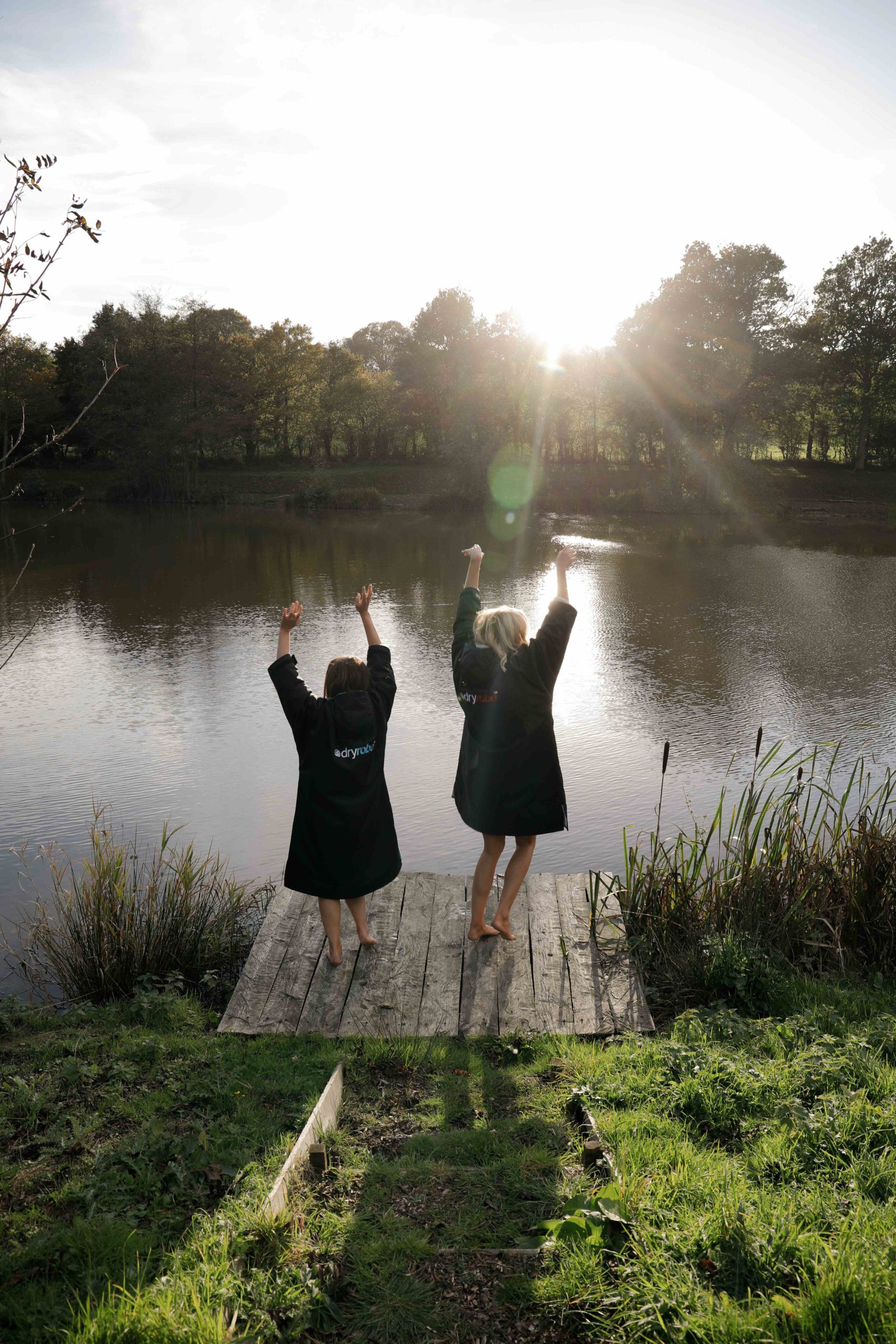 Wild Swimming Essentials: Two women wearing DryRobes next to the edge of a lake