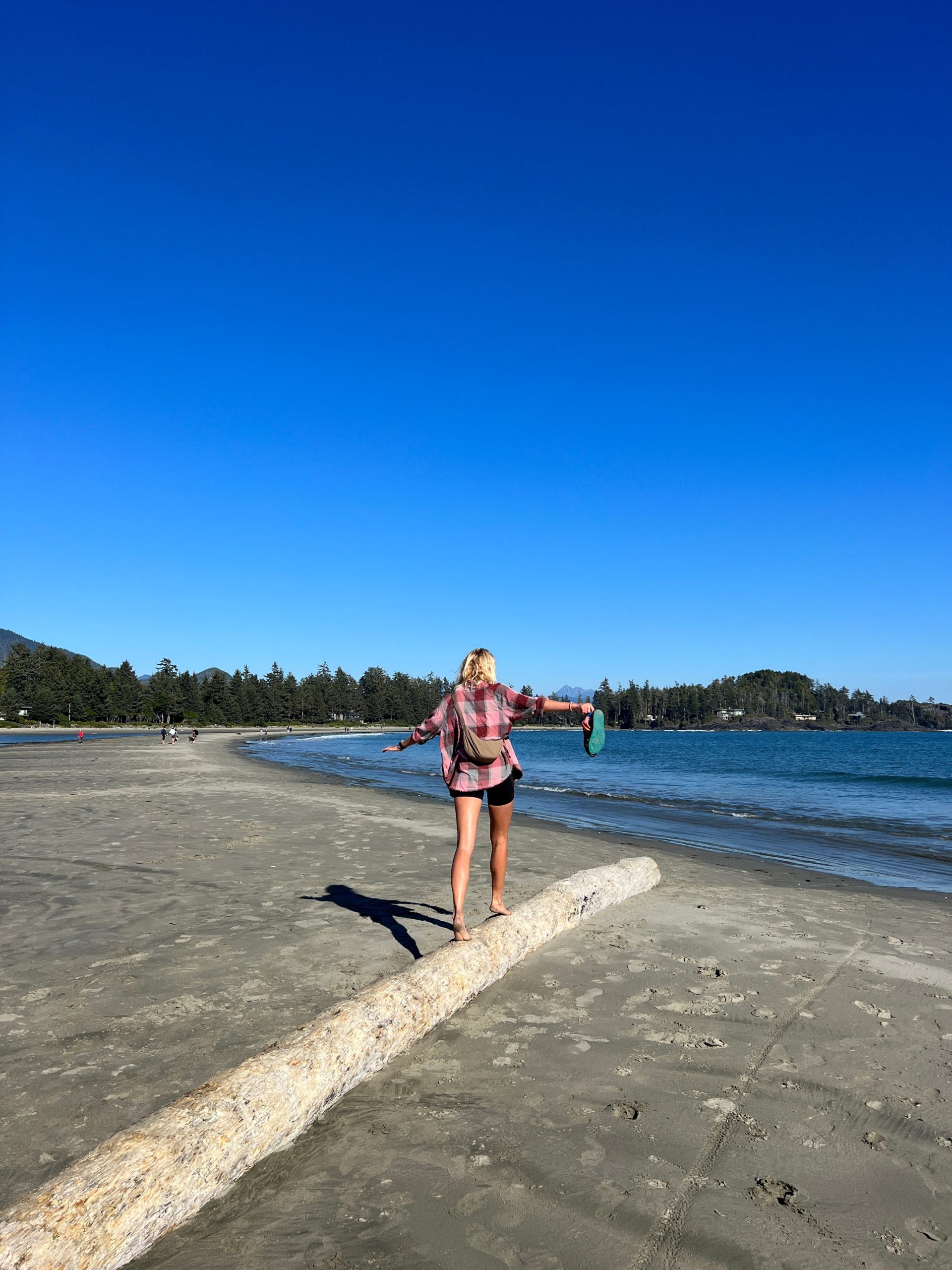 Zanna van Dijk walking along a fallen tree log on a beach in Tofino