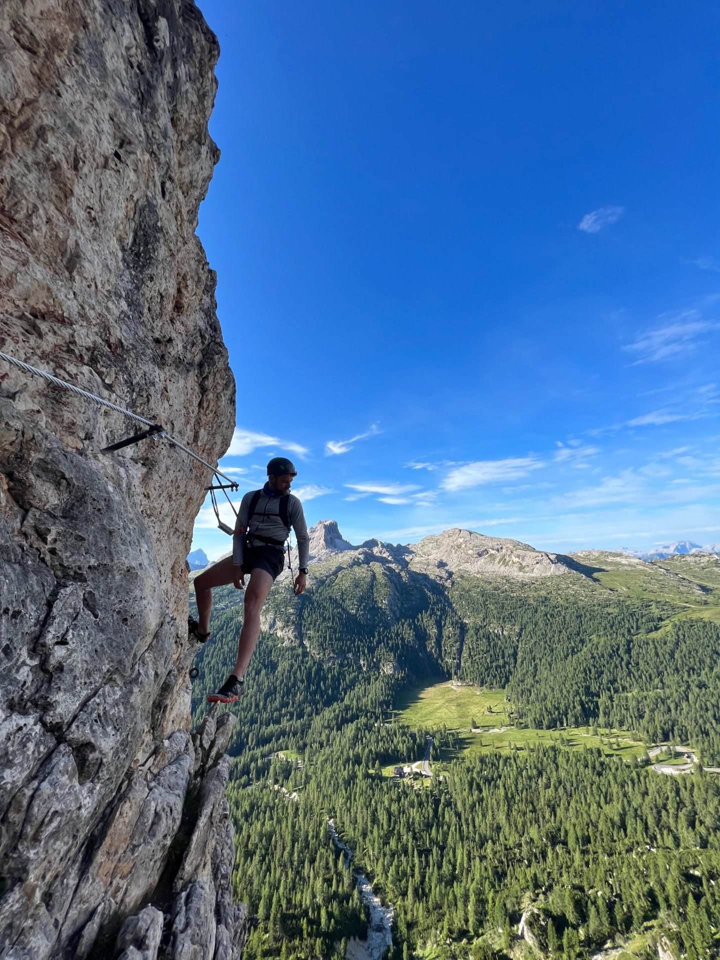 A man sits on the side of a mountain attached to a via ferrata in the Dolomites