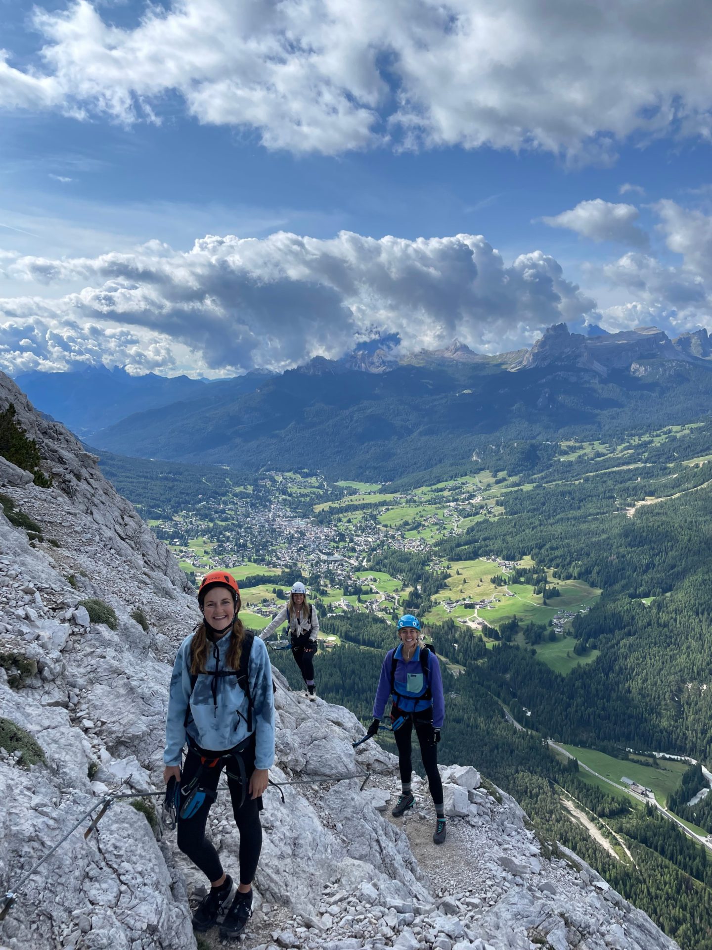 Three women on the side of a mountain in the Dolomites attached to a via ferrata